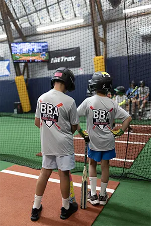 Two players in BBA shirts in the HitTrax batting cage